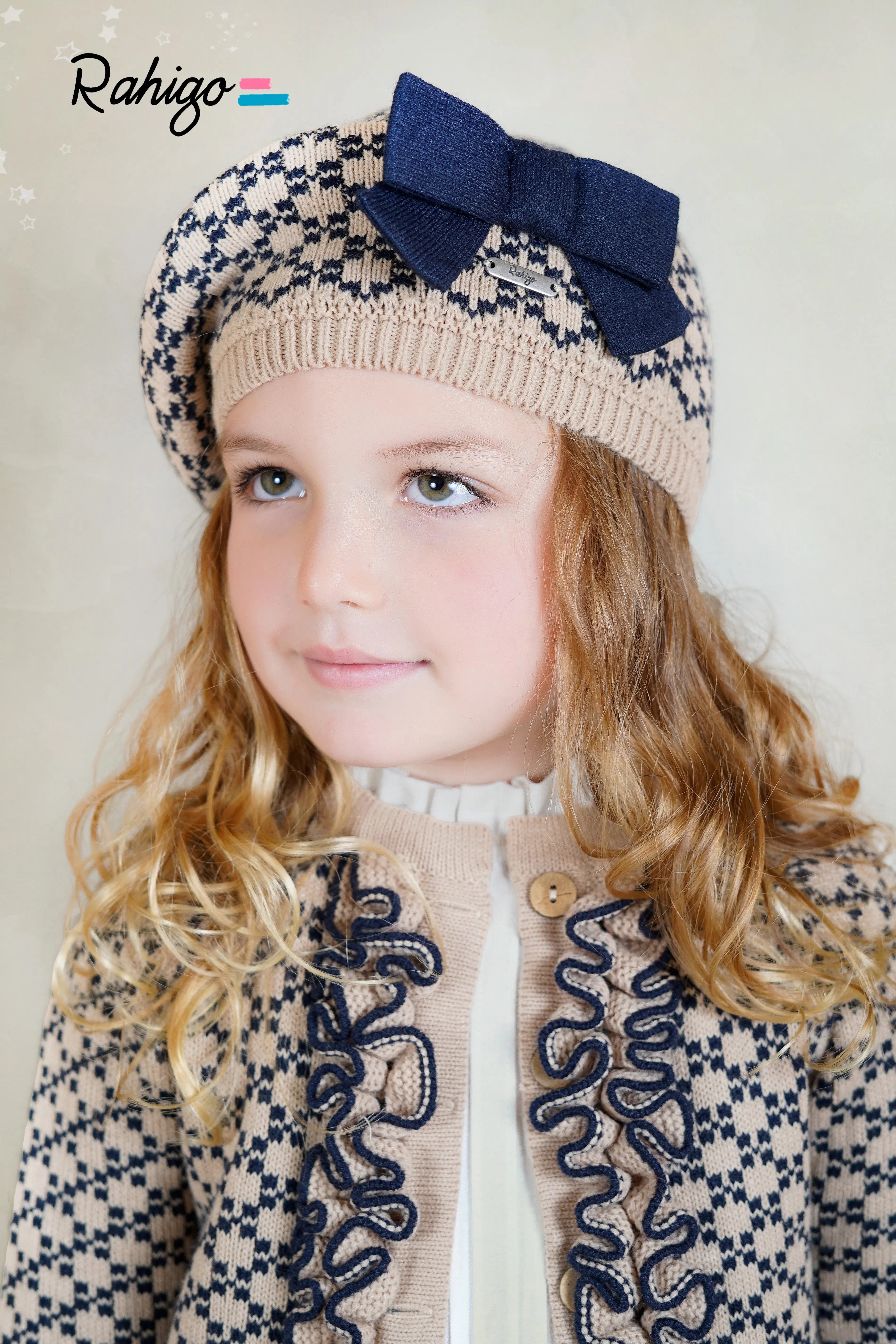 Young girl wearing a patterned coat and hat with a bow, brand 'Rahigo' visible.