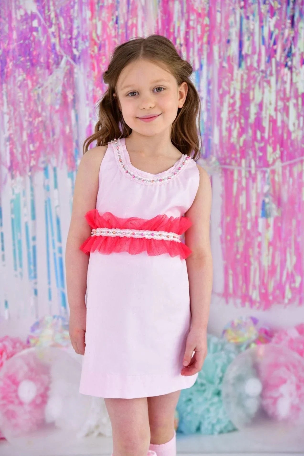 Smiling young girl in pink sleeveless dress with red ruffled belt in colorful party backdrop