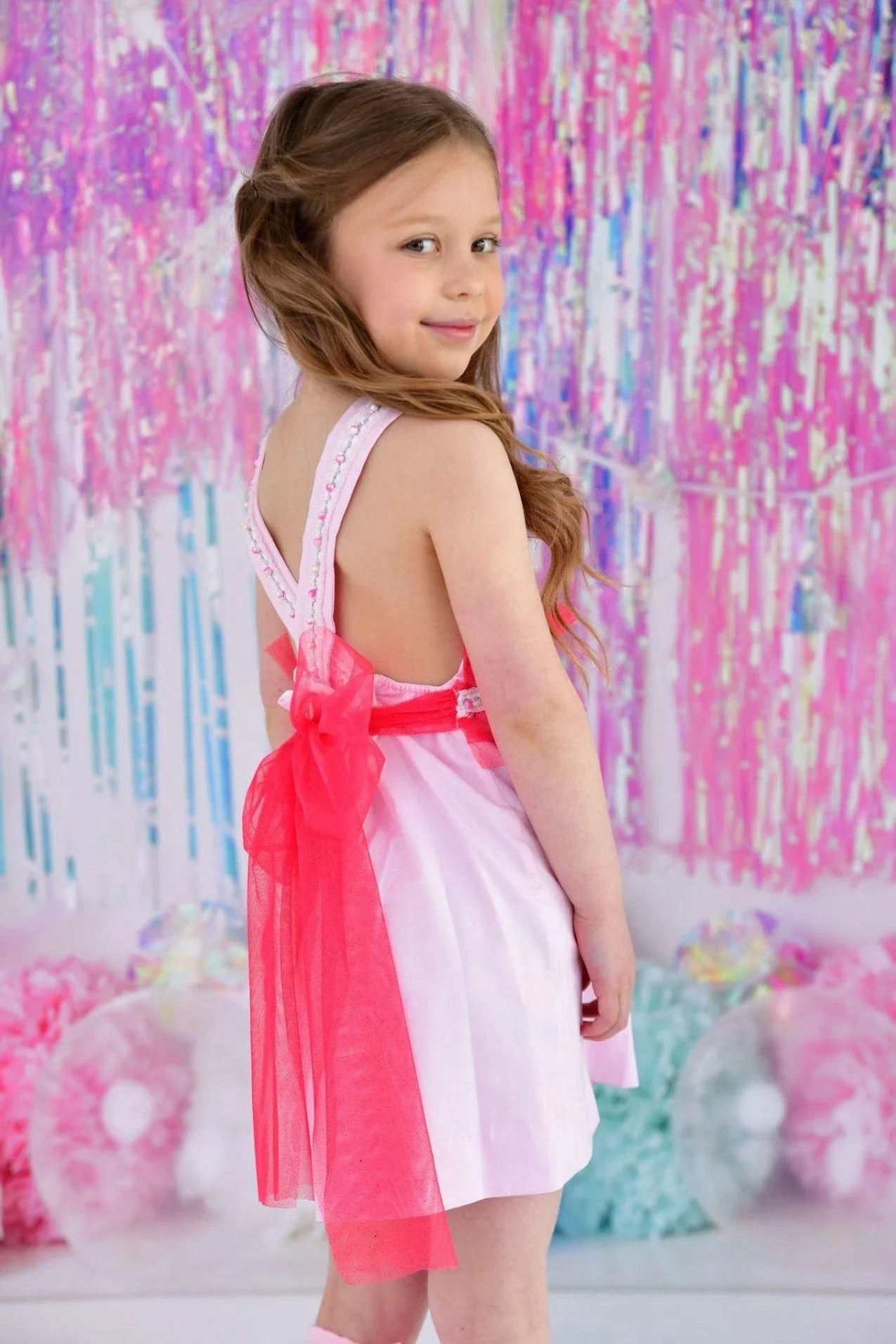 Young girl in pink sleeveless dress with red bow posing against pink and blue party backdrop