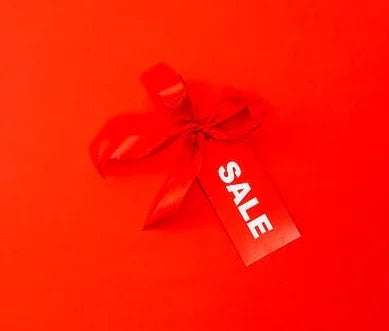 Red sale tag with ribbon on solid red background, minimalist promotional design