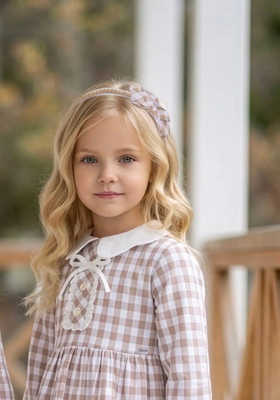AW26 Miranda Girls Beige Gingham Headband with bow design, worn by a girl outdoors. Available in one size (consider sizing up).