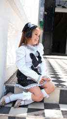 Smiling girl in black and white plaid dress with bows, knee-high socks, and glitter shoes sitting on tiled steps