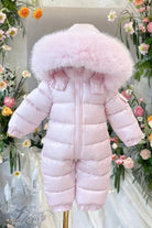 Pink baby snowsuit with fluffy hood displayed on a mannequin surrounded by colorful flowers