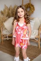 Smiling young girl in colorful patterned romper with pink tulle detail, standing indoors