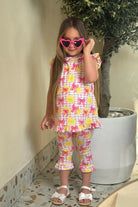 Little girl wearing heart-shaped pink sunglasses and lemon print outfit with pink bows indoors