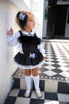 Toddler girl in black and white checkered dress with white blouse, knee-high socks, and gold shoes
