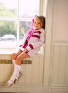 Smiling young girl in pink and white outfit sitting on a sunny window ledge indoors