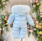 Baby blue padded winter snowsuit with fur-trimmed hood on mannequin, surrounded by colorful flowers