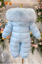 Light blue puffer baby jumpsuit with large fluffy fur hood displayed on mannequin amid floral background