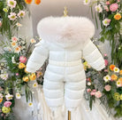 White baby snowsuit with furry hood displayed on mannequin surrounded by colorful flowers