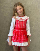 Young girl wearing a red and white vintage dress with lace and polka dots against a textured wall