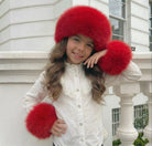 Young girl wearing white blouse with lace and large red fur hat and cuffs, posing outdoors