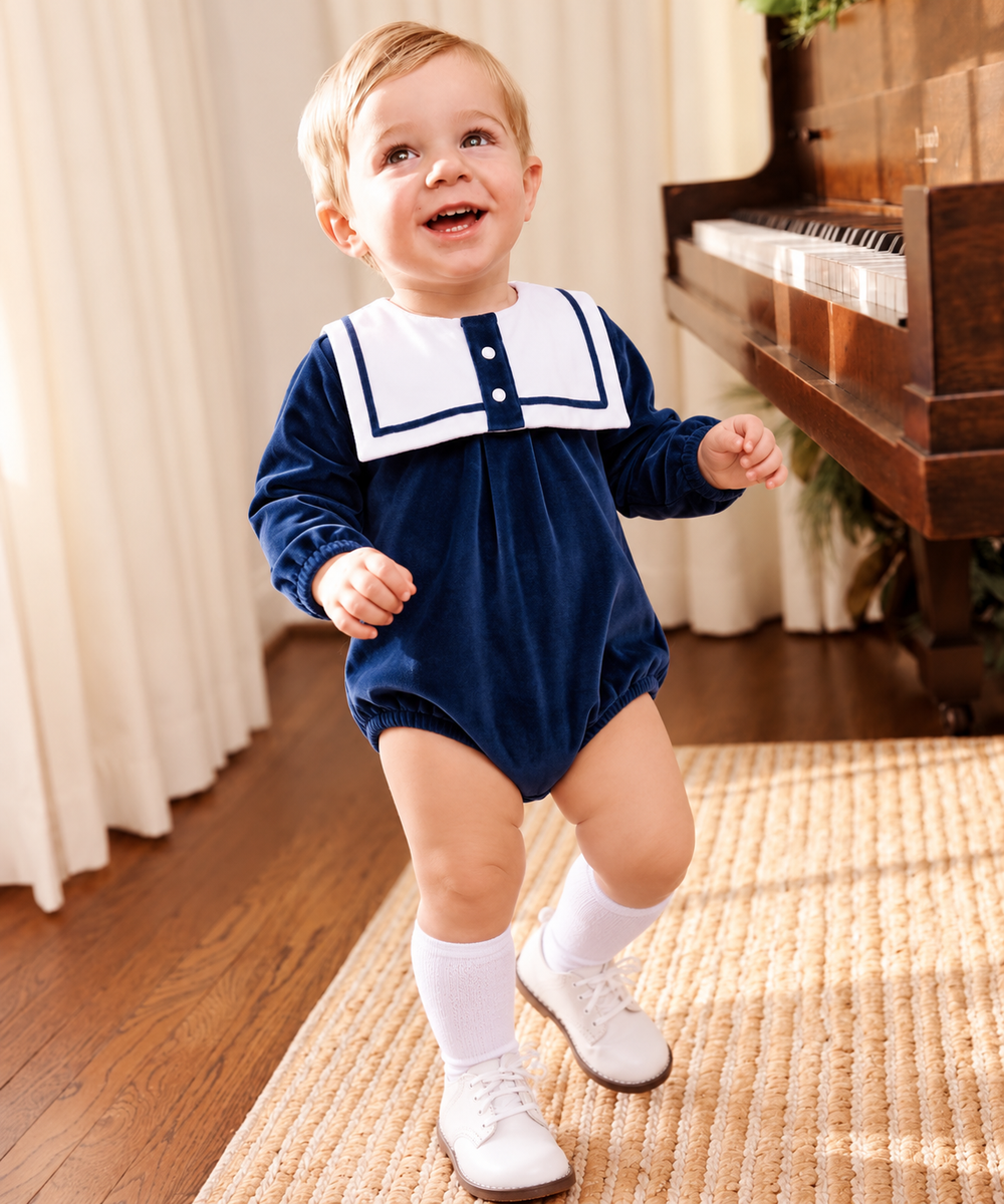 Baby boy wearing a navy blue velour sailor collar romper with white knee-high socks and traditional baby shoes.