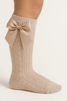 Beige knitted knee-high sock with cable pattern and large satin bow detail