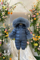 Blue baby snowsuit with large fur hood and cuffs on mannequin surrounded by colorful floral arrangements
