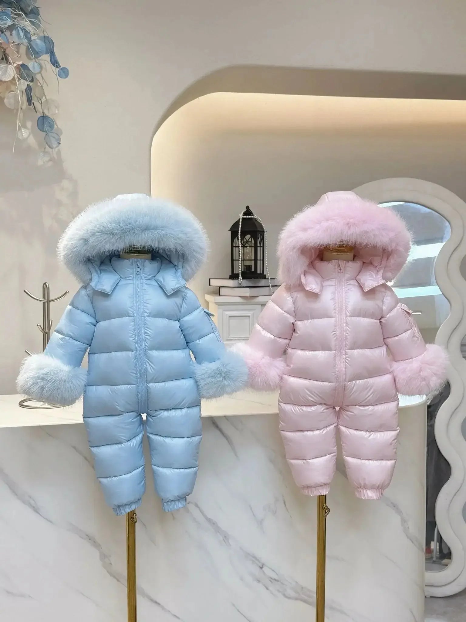 Blue and pink fluffy hooded baby winter snowsuits displayed on mannequins indoors