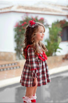 Little girl wearing a red and white plaid dress with matching hair accessory and red stockings outdoors