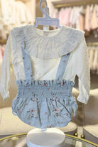 White long-sleeve baby blouse with ruffled collar paired with blue floral suspender skirt on display