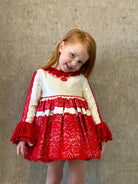 Little girl with red hair wearing white and red lace dress against a textured gray wall