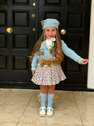 Little girl in stylish blue knit hat, sweater with gold accents, tweed skirt, knee-high socks, and white shoes