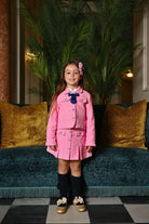 Young girl wearing pink skirt suit with navy bow and headband, standing in elegant living room
