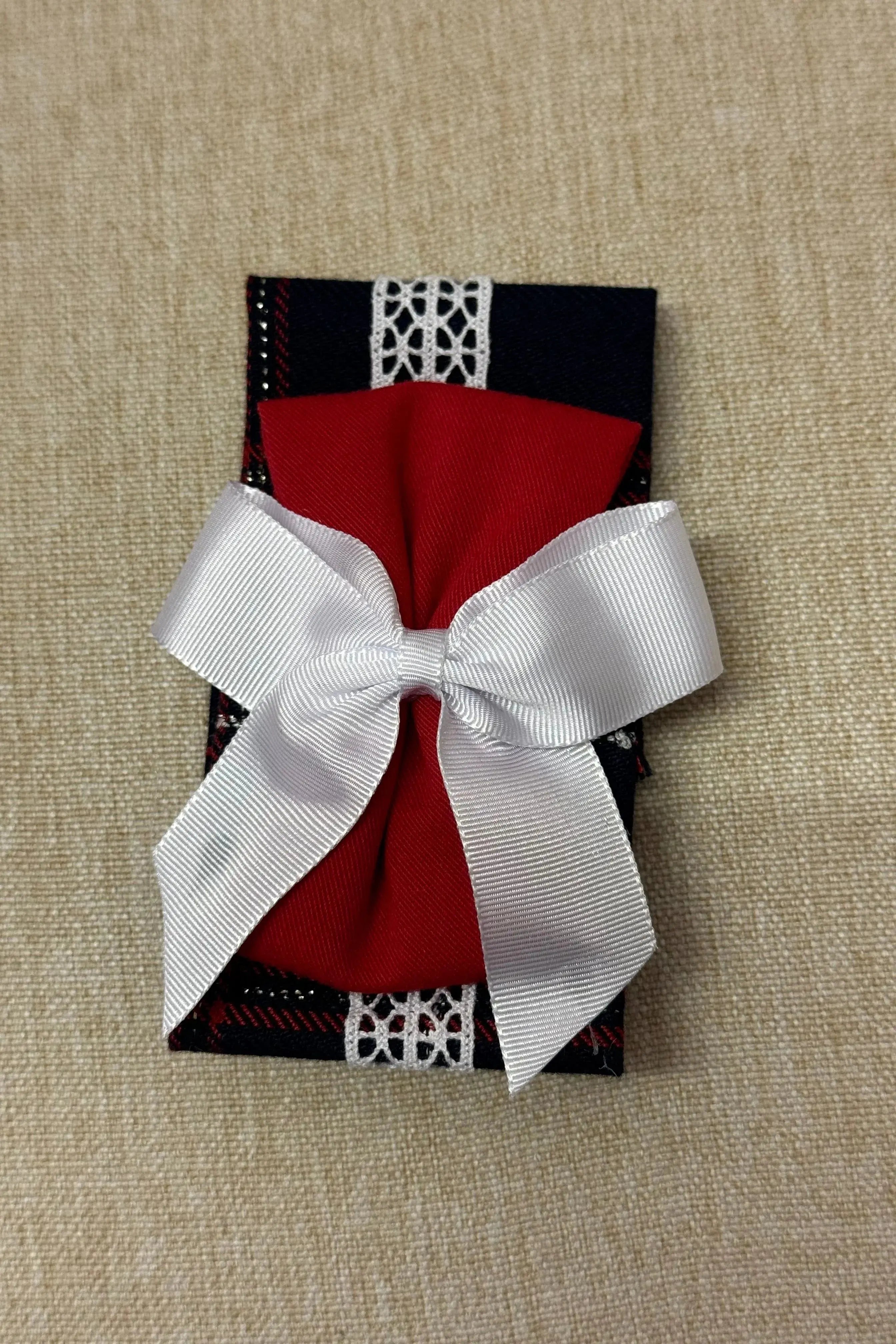 Red fabric bow hair accessory with white ribbon on navy blue check fabric background