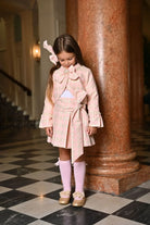 Little girl in pink houndstooth blazer and skirt set with bow details, standing on black and white checkered floor
