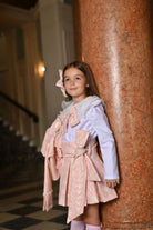 Young girl in pink houndstooth skirt and blazer set, white blouse, standing by marble column indoors