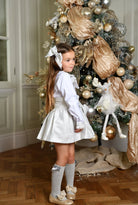 Girl in silver croc hair bow, white blouse, and silver skirt standing by elegant Christmas tree