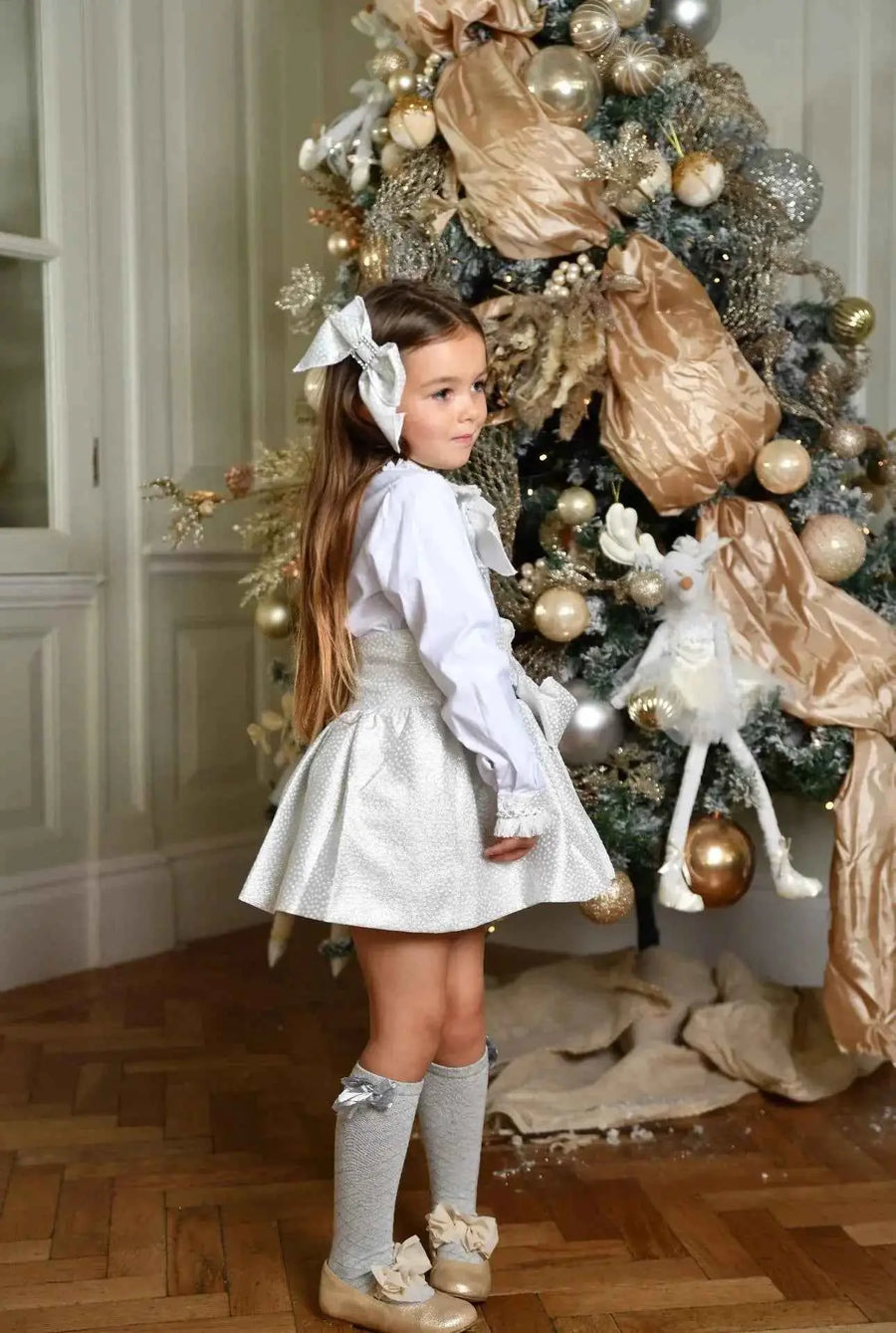 AW26 Naxos Girls Silver Croc Hair Bow, handmade in Spain, available in sizes 4 to 12 years, worn by a girl next to a Christmas tree.