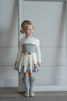 Young girl wearing a white and grey London-themed dress with knee-high socks and gold shoes, standing indoors