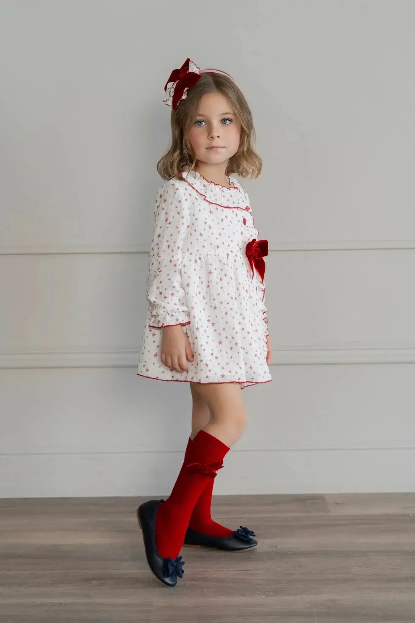 Young girl in white dress with red stars and bow, red knee-high socks, and navy blue shoes