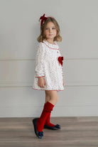 Young girl in white dress with red stars and bow, red knee-high socks, and navy blue shoes