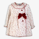 White baby dress with red star pattern, ruffled collar, red buttons, and large red velvet bow