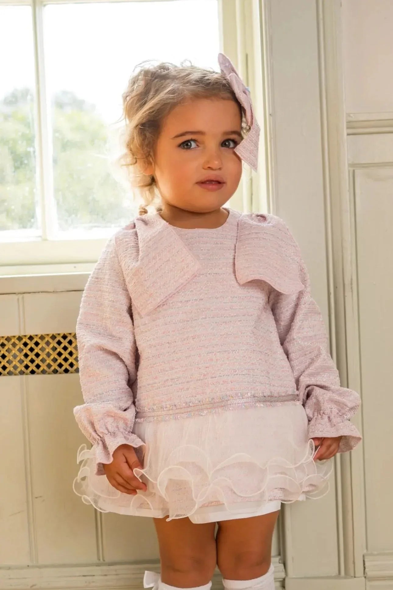 Toddler girl in pink textured dress with ruffled hem and matching headband standing indoors
