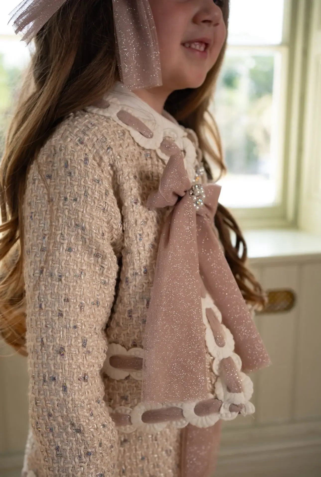 Close-up of girl wearing beige tweed jacket with large sparkling pink bow and floral details