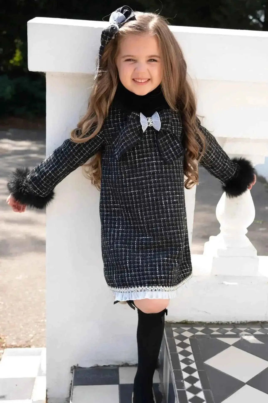 AW26 Naxos Girls Black Fur Tweed Dress with bow detail, available in sizes 4-14 years.