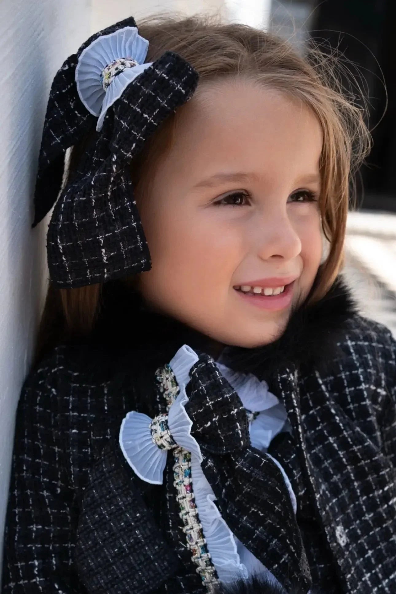 Smiling young girl wearing a black and white tweed bow and coat with fur collar detail