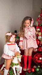 Two young girls in festive red and white outfits near decorated Christmas tree with ornaments and nutcracker toys