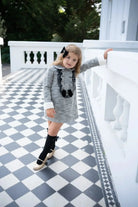 Young girl wearing black tweed dress with bows, black knee-high socks, and gold shoes on tiled patio