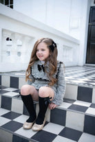 Little girl in black tweed short set with bows sitting on black and white checkered stairs