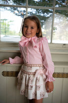 Smiling girl in pink blouse with bow and carousel print skirt indoors by window