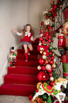 Young girl in festive red and white outfit running down red-carpeted stairs decorated with Christmas ornaments and nutcracker figures