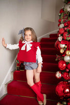 Young girl in red sleeveless jumper, white blouse, striped shorts, red knee socks on red carpeted stairs with Christmas decor