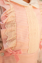 Close-up of pink gingham pinafore dress with lace trim and pink velvet bow detail