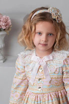 Young girl with blonde hair wearing a pink and blue patterned dress with lace collar and headband