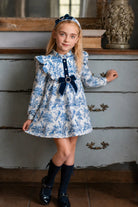 AW26 Rochy girls blue and ivory toile print A-line dress with navy velvet bow, pearl details and ruffle shoulders, sizes 4 to 14 years
