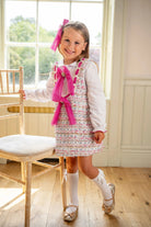 Smiling young girl in pink bow and tweed dress with white blouse, knee-high socks, and glitter shoes indoors