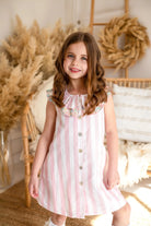 Smiling girl in pink and white striped dress with floral collar in cozy boho room