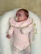 Baby in pink knit outfit with large collar lying in white DockATot Deluxe+ baby lounger
